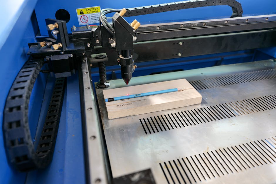 A laser cutter machine in operation, with a computer screen nearby showing the digital file being prepared for cutting wood.
