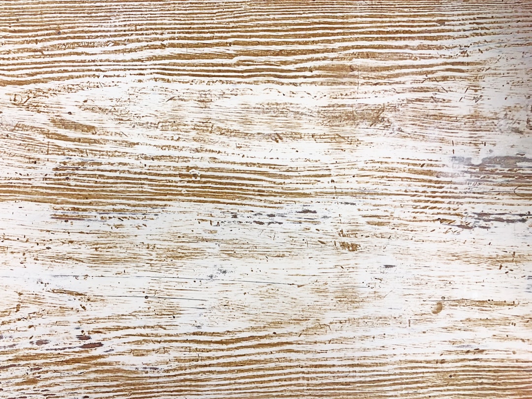 Hands using a wire brush attachment on a drill to distress a piece of pine wood, creating a rustic, weathered texture.
